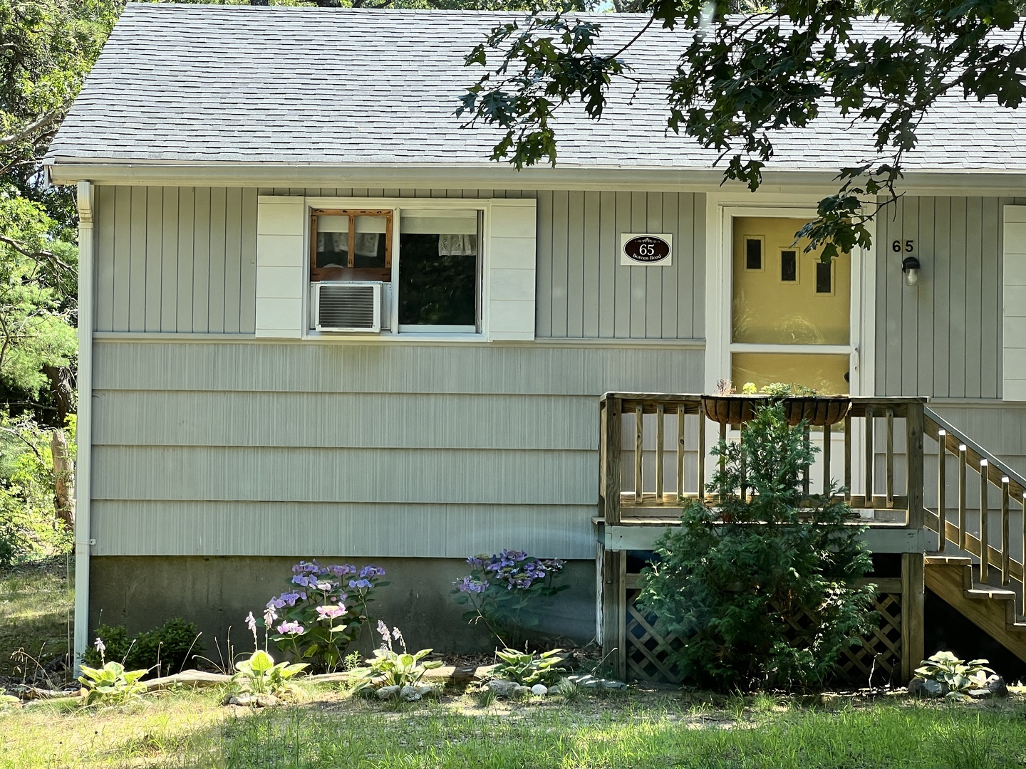 Charming cottage exterior with elevated entrance, surrounded by mature trees and colorful garden plantings in a peaceful neighborhood setting.