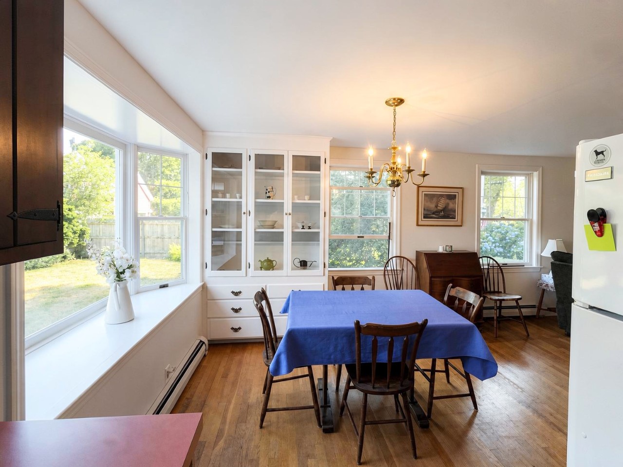 Gather around this inviting dining space where warm hardwood floors and charming vintage touches create a cozy atmosphere. Sunlight pours through large windows overlooking the peaceful yard, perfect for your morning coffee or evening meals.