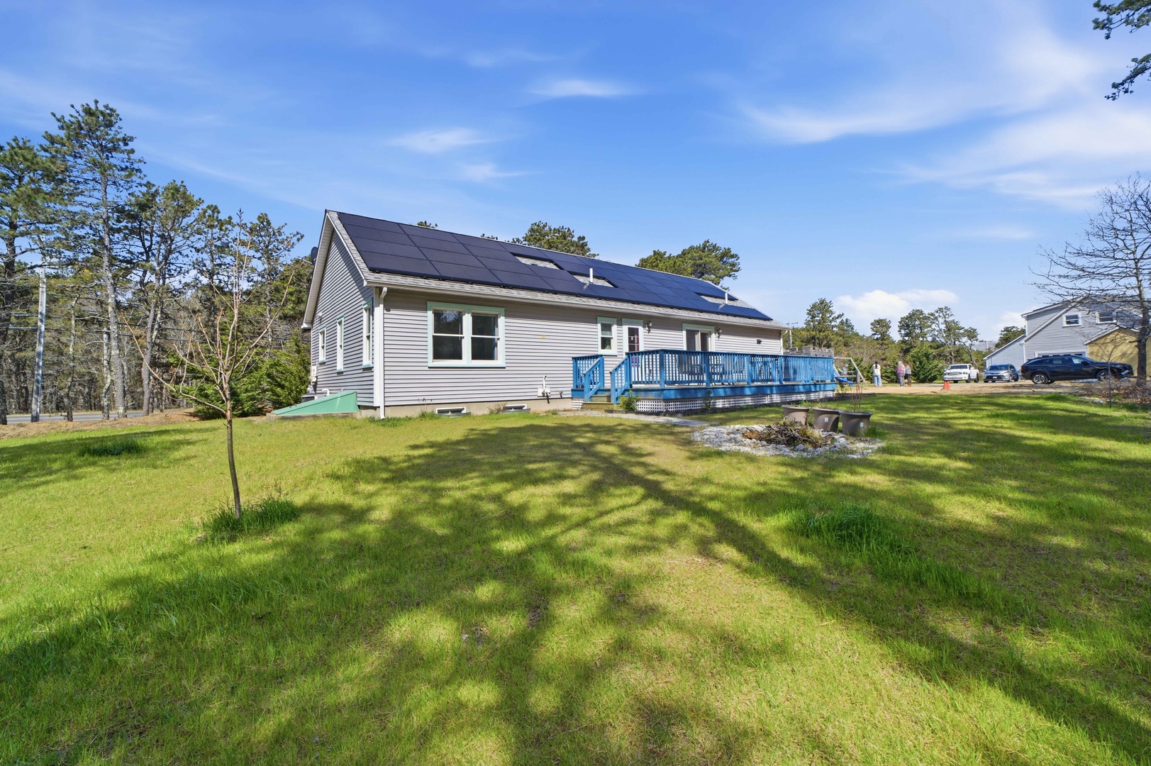 Eco-friendly vacation home with solar panels sits on expansive green lawn surrounded by mature trees and wooded privacy.