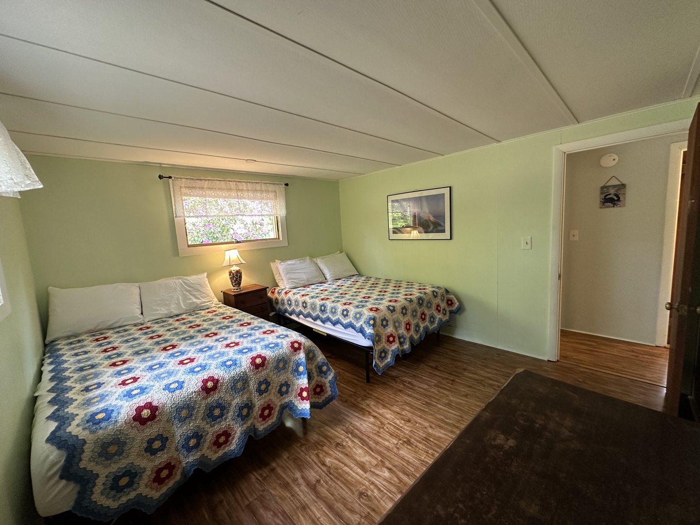 Your cozy bedroom features two comfortable beds with handmade quilts, warm lighting, and a peaceful garden view.