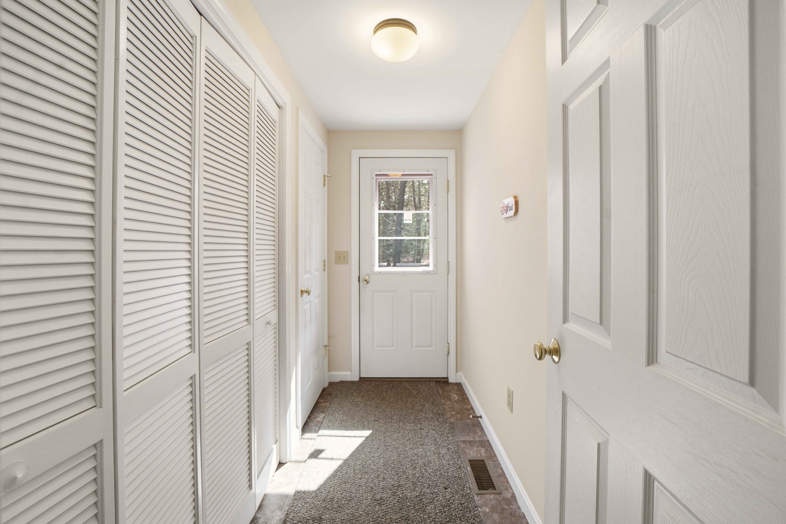 Step into your private entryway with abundant storage space. White louvered closets line the hallway, keeping your belongings organized while natural light streams through the door's window.