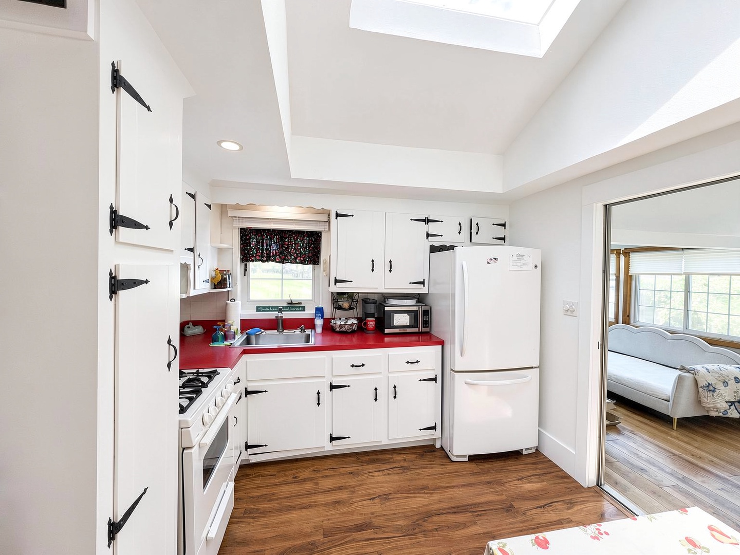 Your charming kitchen features vintage-style white cabinetry with bold red countertops, modern appliances, and a skylight flooding the space with natural light—ready for home-cooked meals.