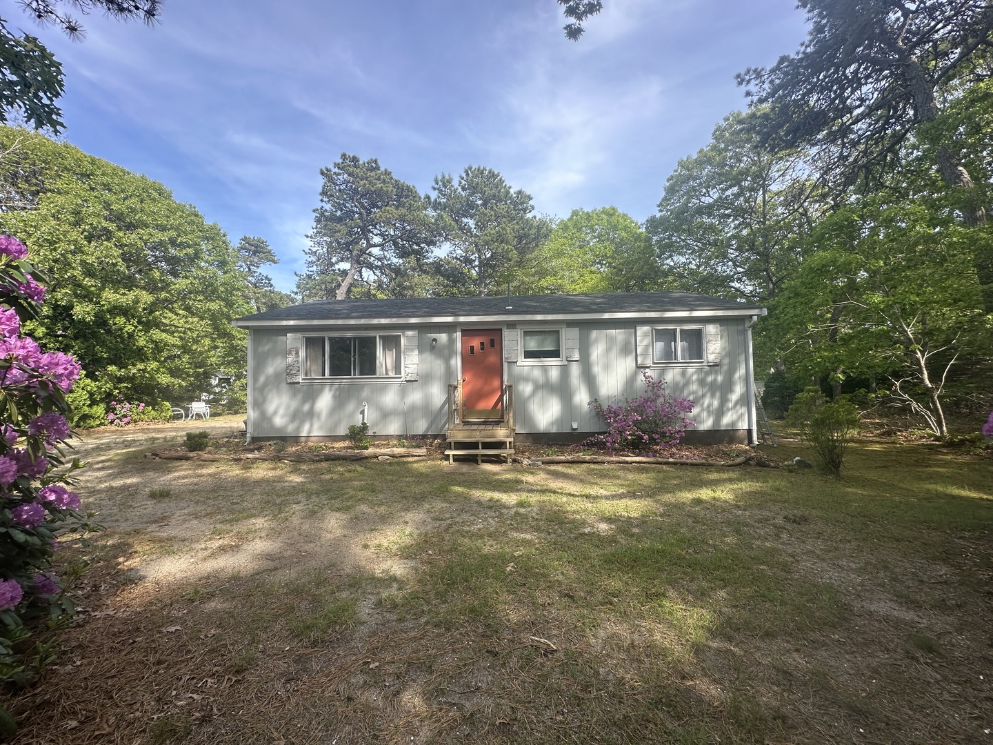 A charming single-story retreat nestled among mature trees, featuring vibrant blooming azaleas and a welcoming orange front door.