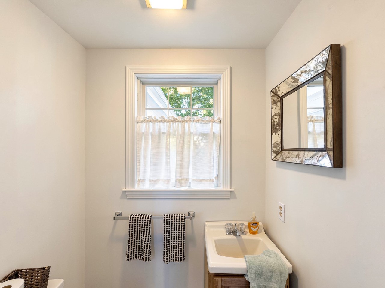 A bright, clean bathroom awaits you with fresh towels, natural light, and a rustic mirror adding character. Practical and charming for your daily routine.