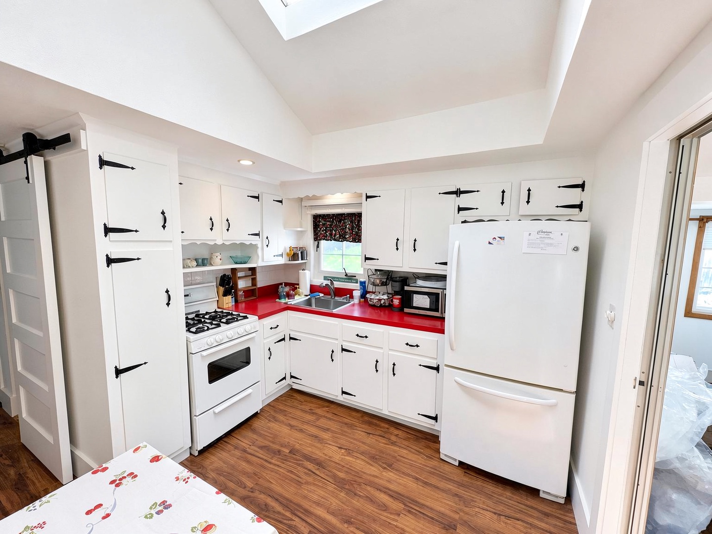 Your charming kitchen features vintage-inspired white cabinetry with bold red countertops, full-sized appliances, and a cozy skylight that fills the space with natural warmth.
