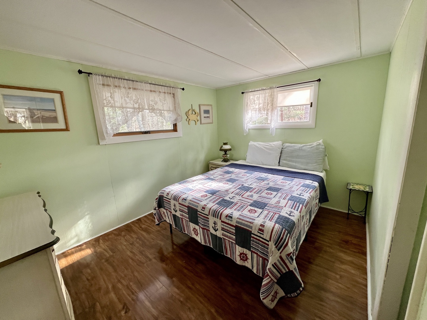 Drift into peaceful sleep in your cozy bedroom with cheerful green walls, nautical quilted bedding, and natural light streaming through lace-curtained windows.