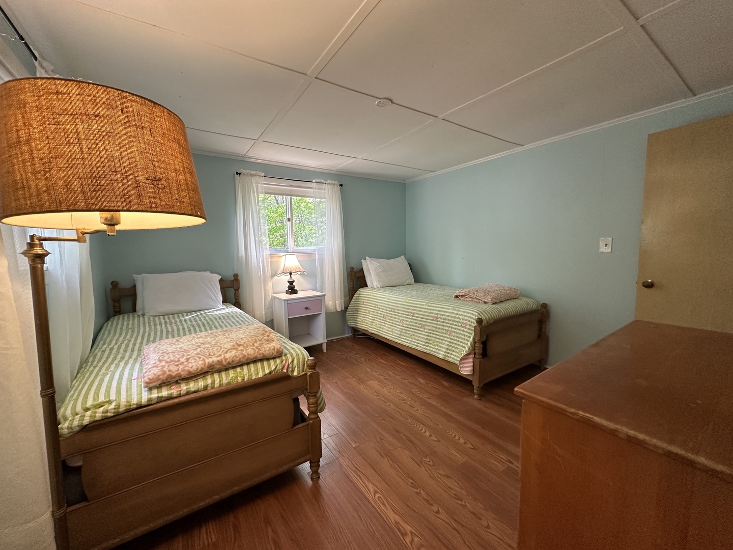 Rest peacefully in this charming twin bedroom with soft green walls, warm wood floors, and natural light streaming through your window.
