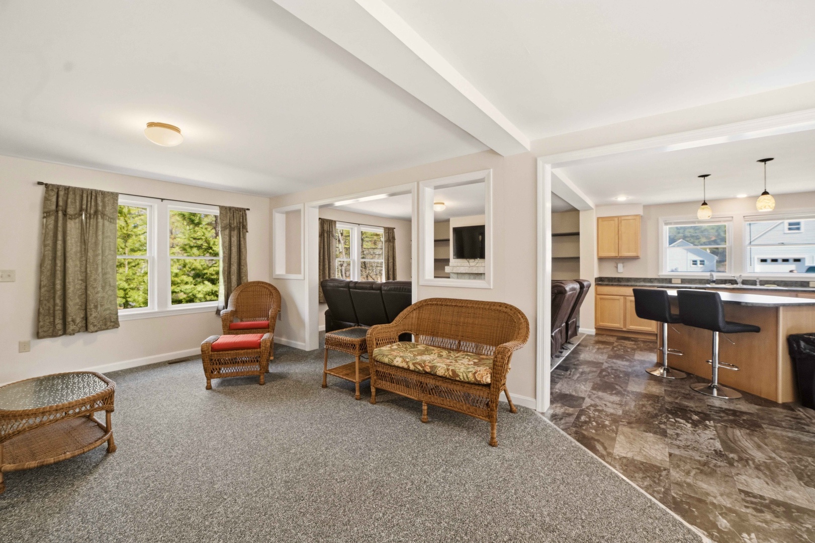 Relax in your spacious open-plan living area with wicker seating, modern kitchen, and peaceful garden views through large windows.