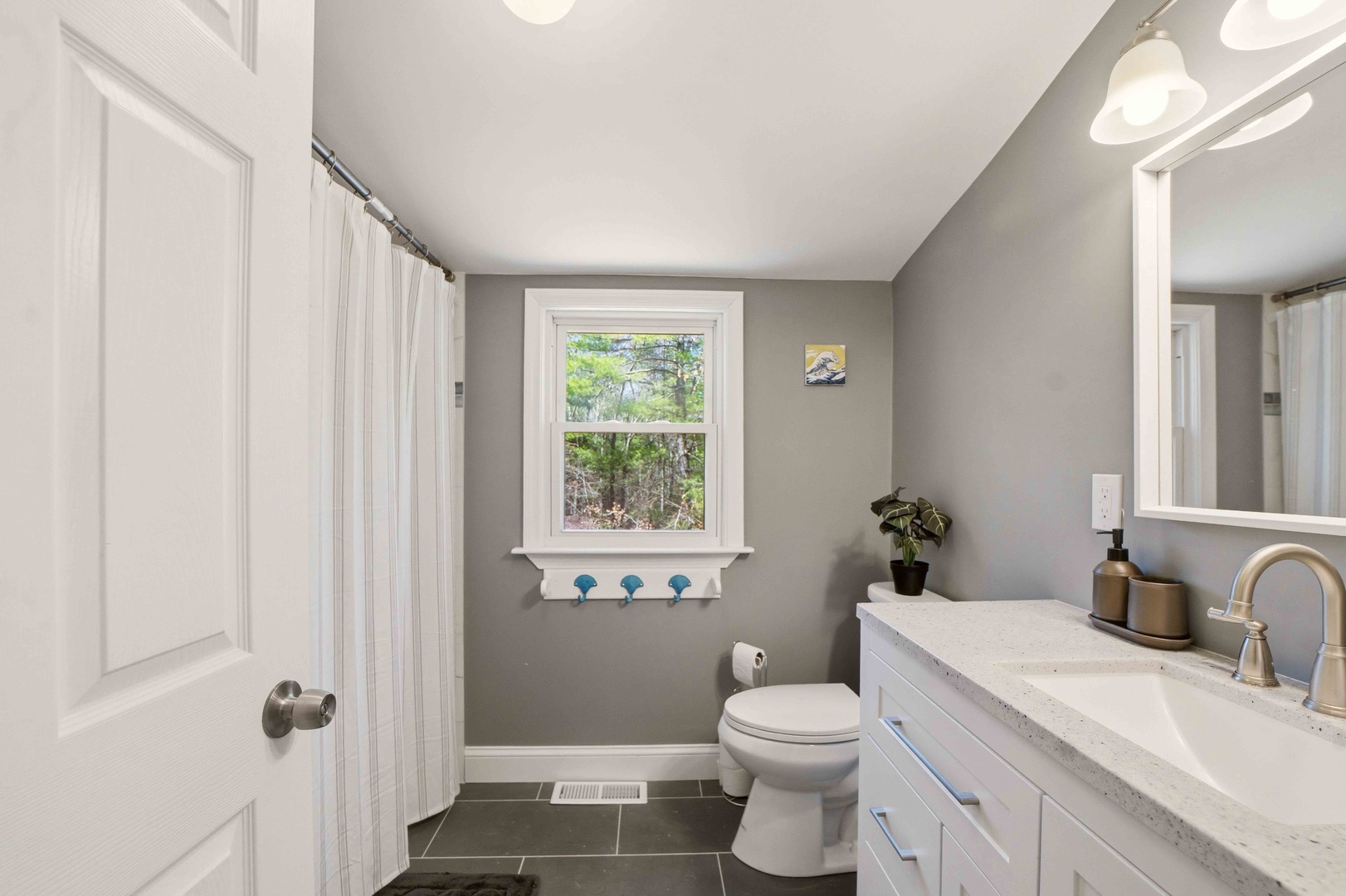 Refresh in your stylish bathroom with modern fixtures, marble counters, and peaceful garden views through the bright window.