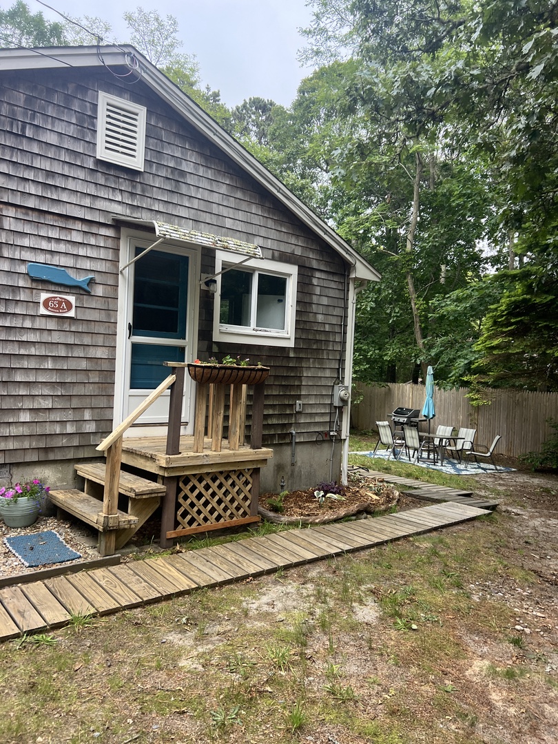 Charming cottage exterior featuring a welcoming wooden deck with outdoor seating surrounded by mature trees and natural landscaping.