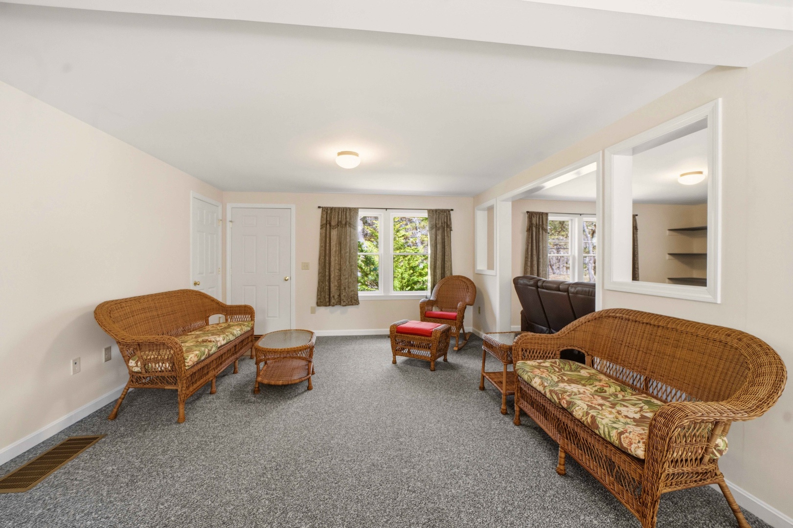 Unwind in your spacious living room with charming wicker furniture and peaceful garden views through bright windows.