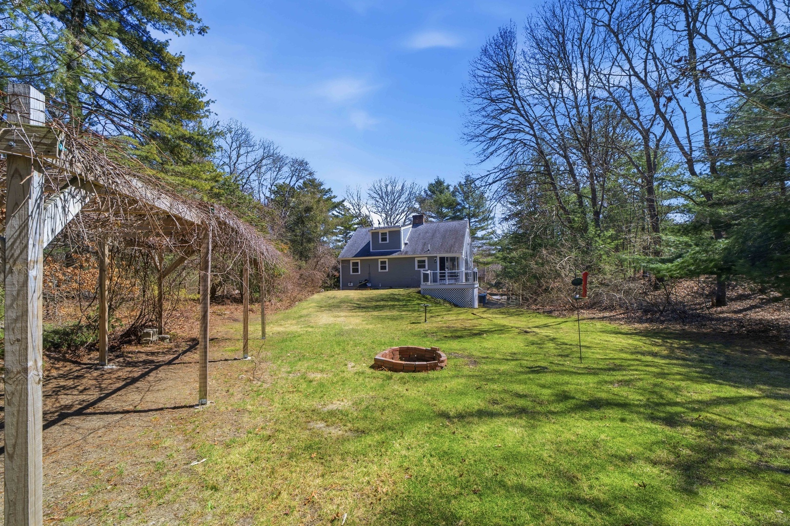 Charming property nestled among mature trees with expansive lawn and fire pit for peaceful outdoor gatherings.