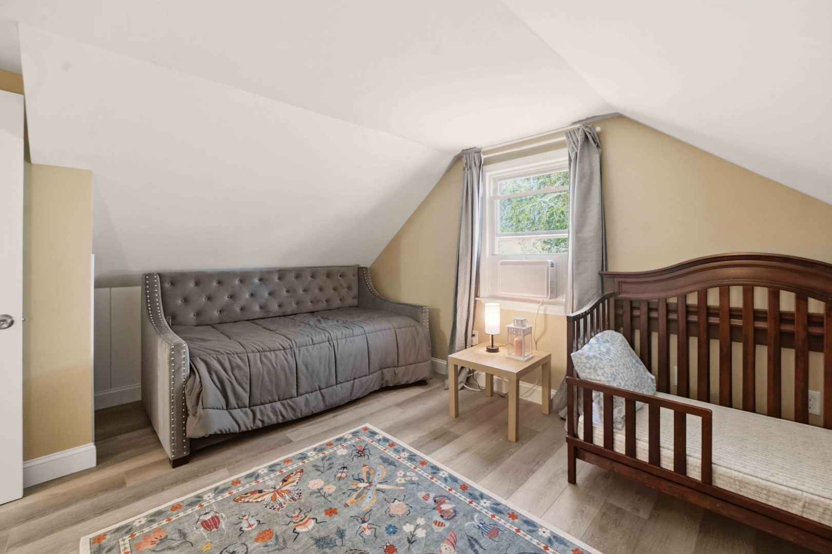 Cozy attic space perfect for your little ones, featuring a comfortable daybed and crib under charming slanted ceilings with natural light streaming in.