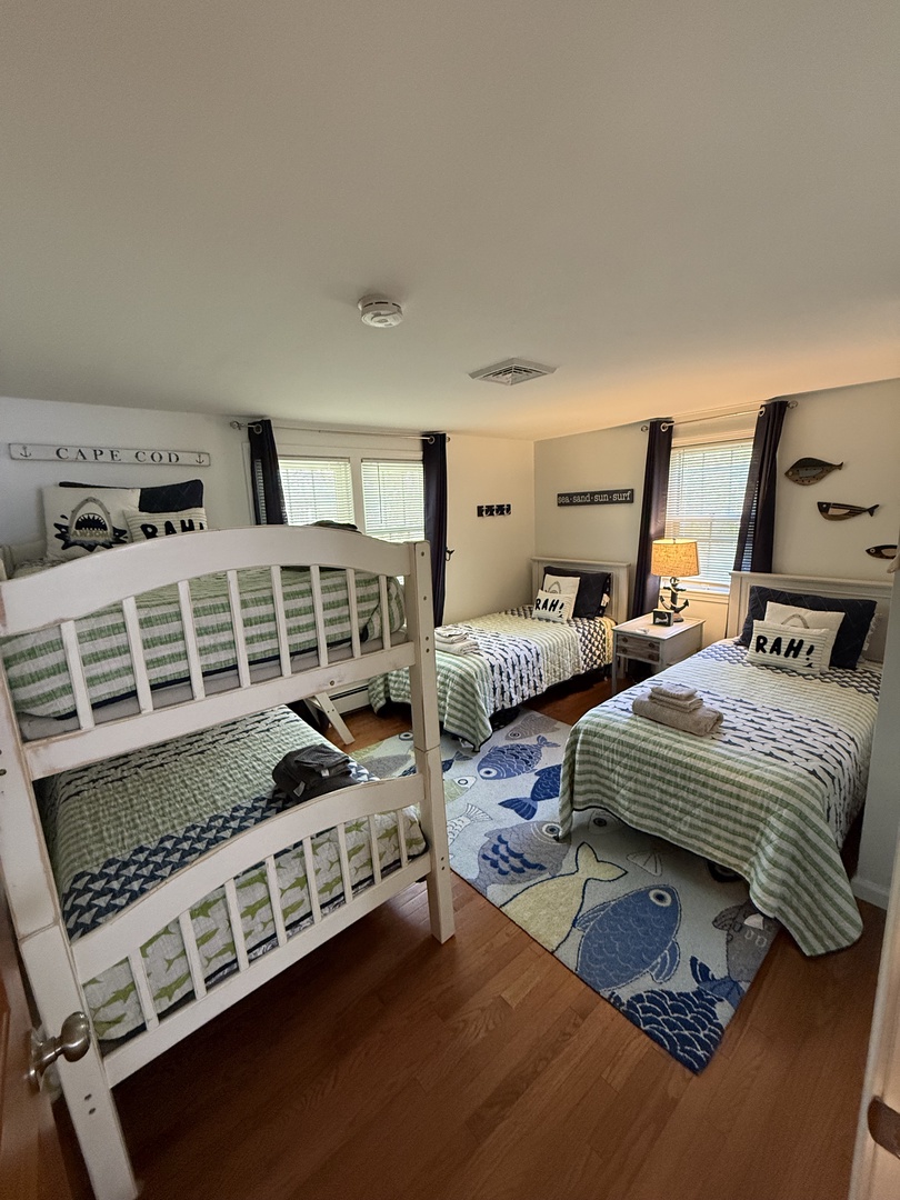 Your coastal-inspired bedroom awaits with cheerful striped linens, playful fish accents, and warm wood floors that set a relaxed, beachy tone for restful mornings.