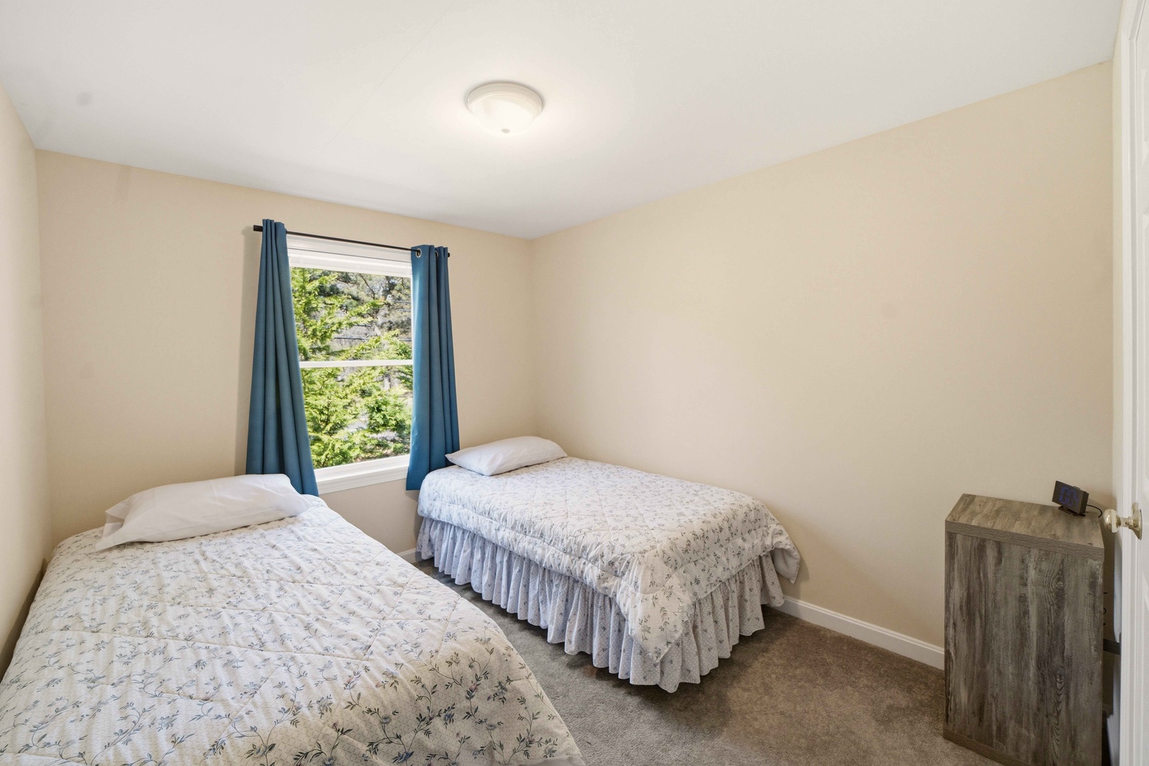 Your cozy twin bedroom offers peaceful garden views through cheerful blue curtains, perfect for a restful night's sleep.