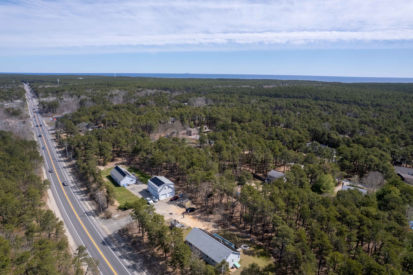 Aerial view of wooded neighborhood with scattered homes nestled among mature trees near main road access.