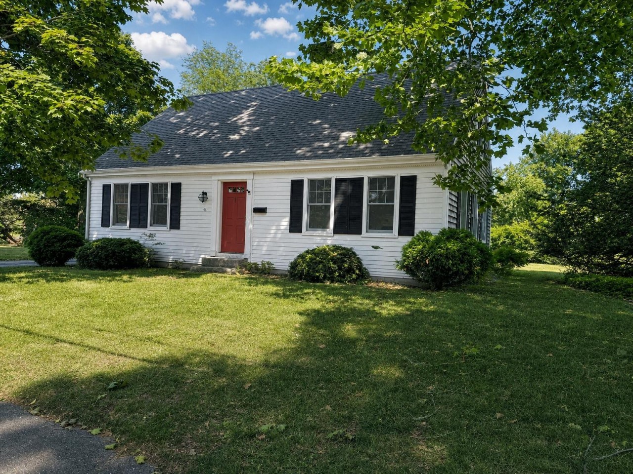 Charming white cottage nestled among lush trees, offering a peaceful retreat with classic curb appeal and a welcoming red door marking the entrance to the property.