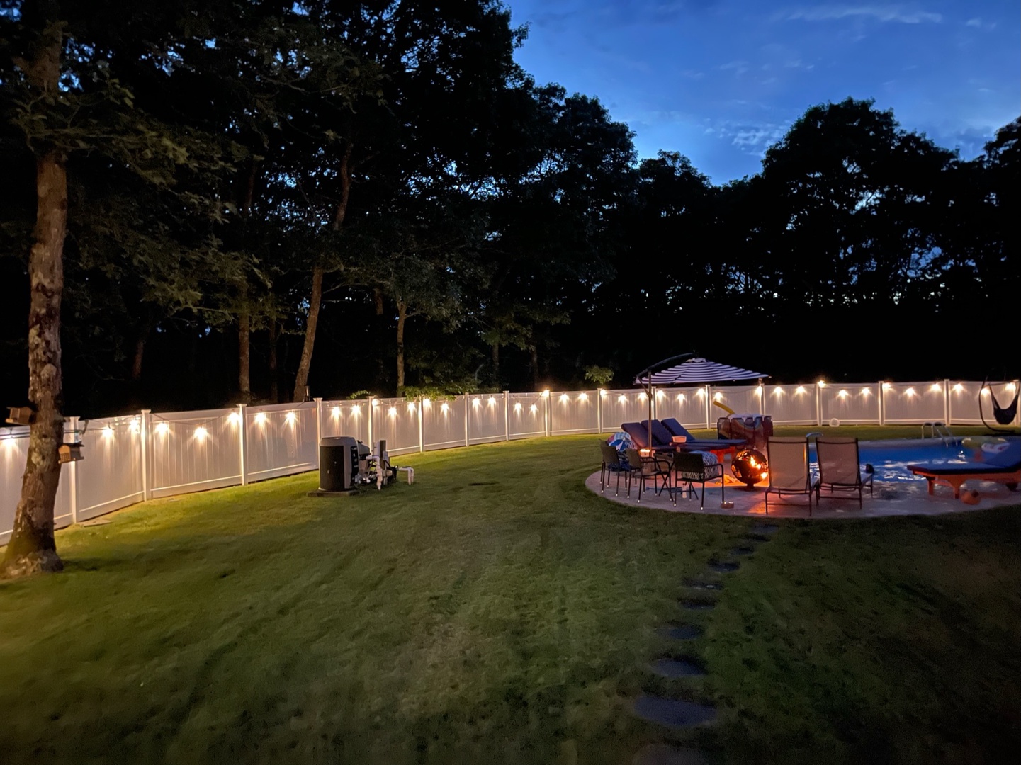 Step into your private backyard oasis where string lights create magical ambiance above your patio and sparkling pool at twilight.