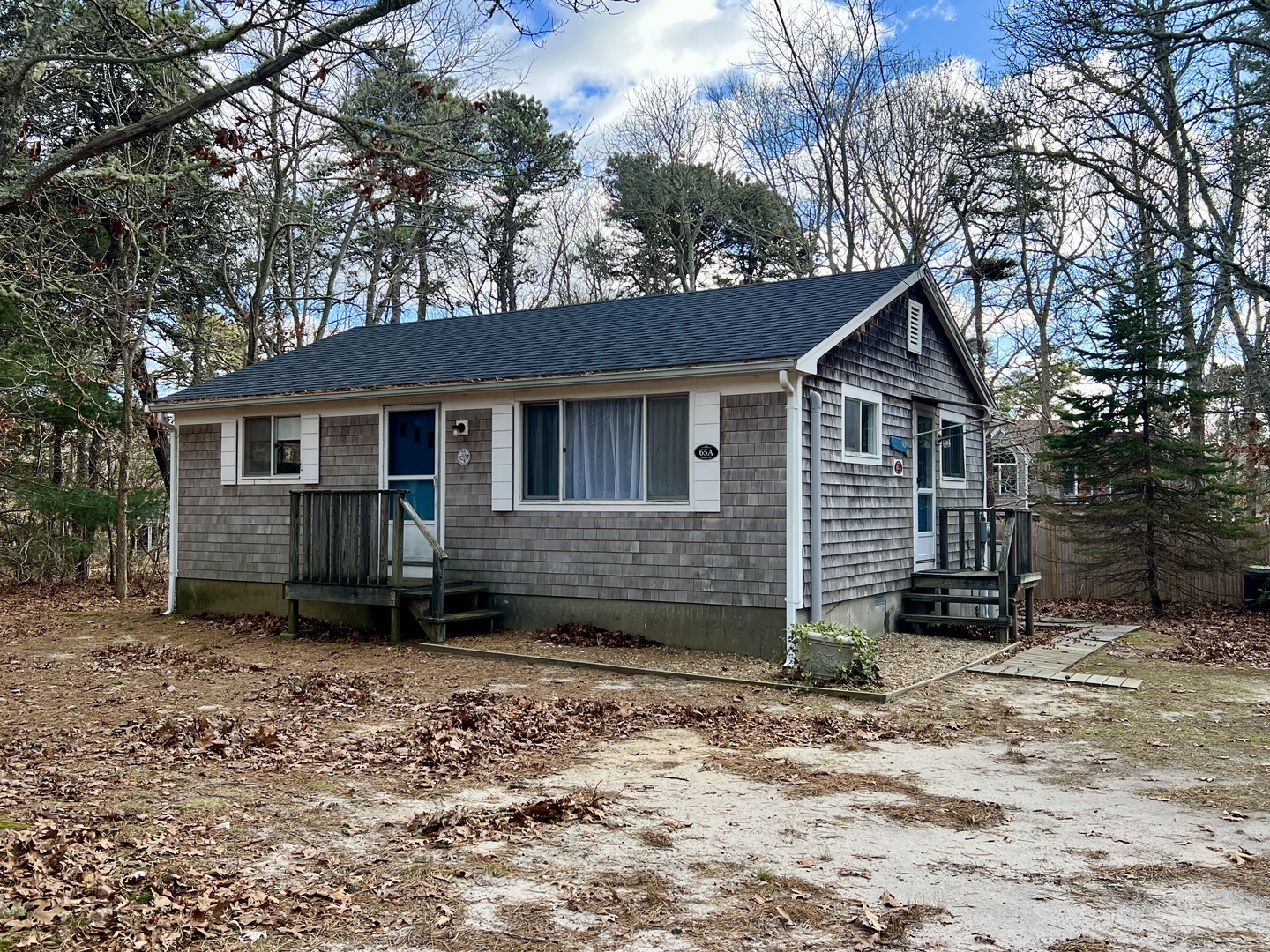 Charming cedar-shingled cottage nestled among mature trees, offering a peaceful woodland retreat with classic New England character.
