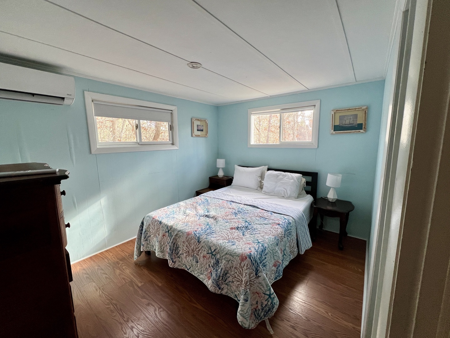 Drift off peacefully in this serene bedroom with soft blue walls and natural light streaming through dual windows.