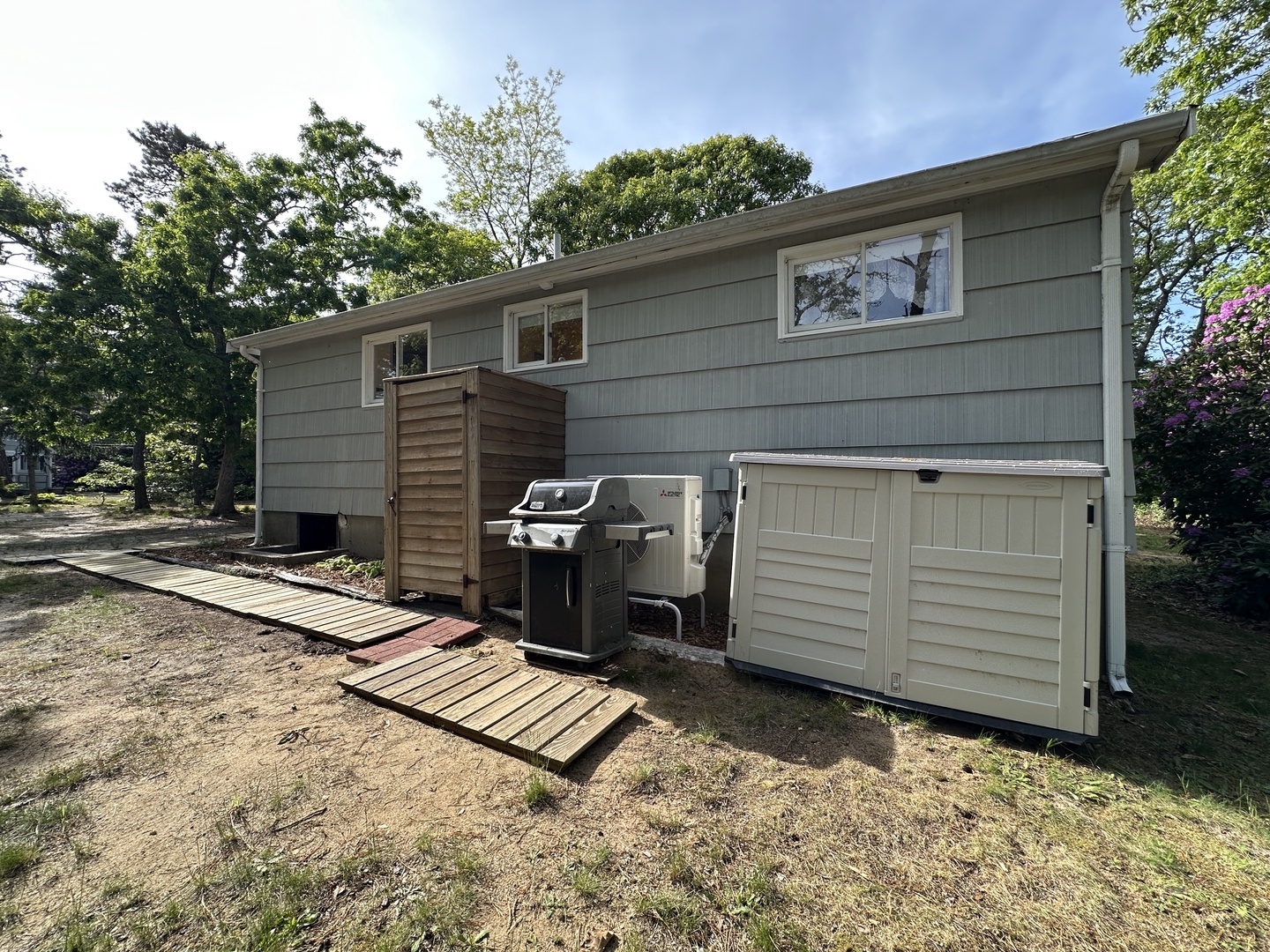 Modern vacation rental exterior featuring BBQ grill and storage shed, surrounded by mature trees in a peaceful neighborhood setting.