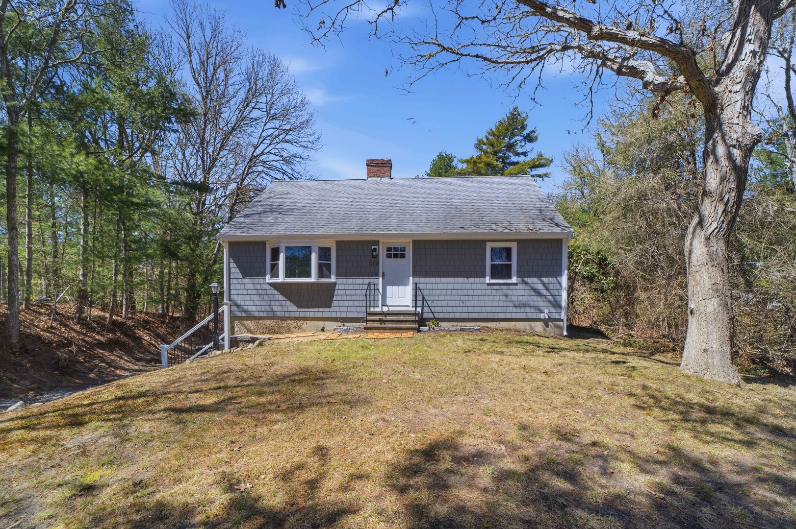 Charming cottage nestled among mature trees with a welcoming front entrance and peaceful wooded setting.