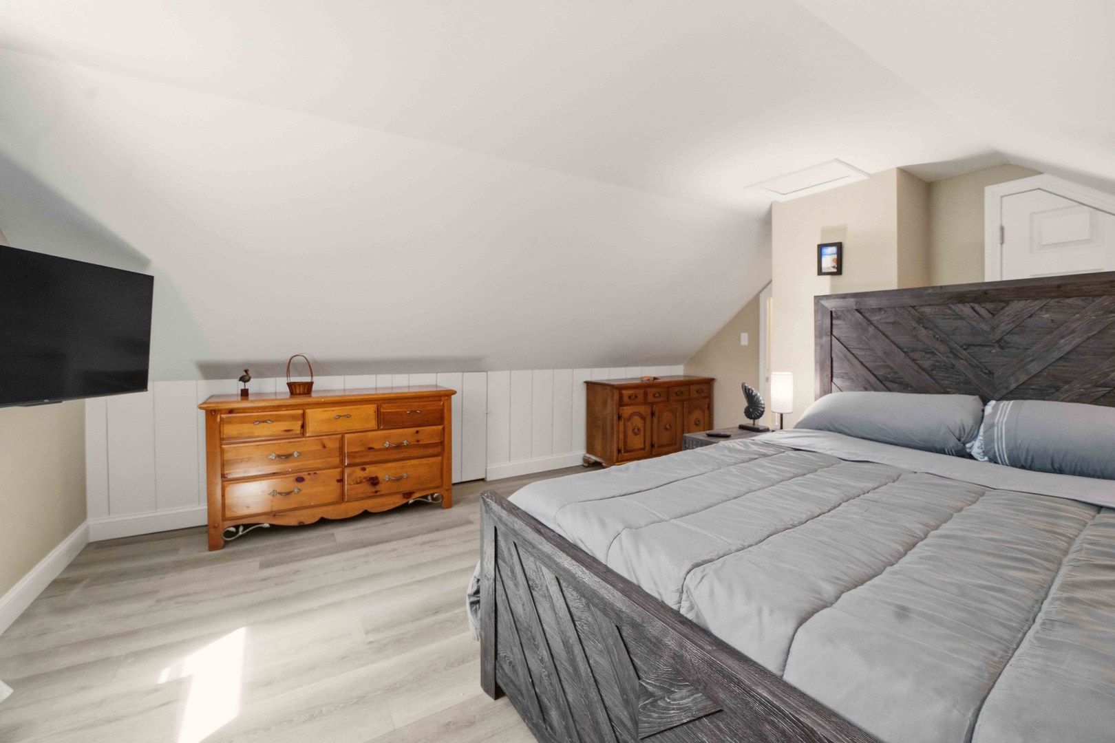 Relax in your peaceful loft bedroom, featuring rustic wood furnishings and modern comforts beneath sloped ceilings.