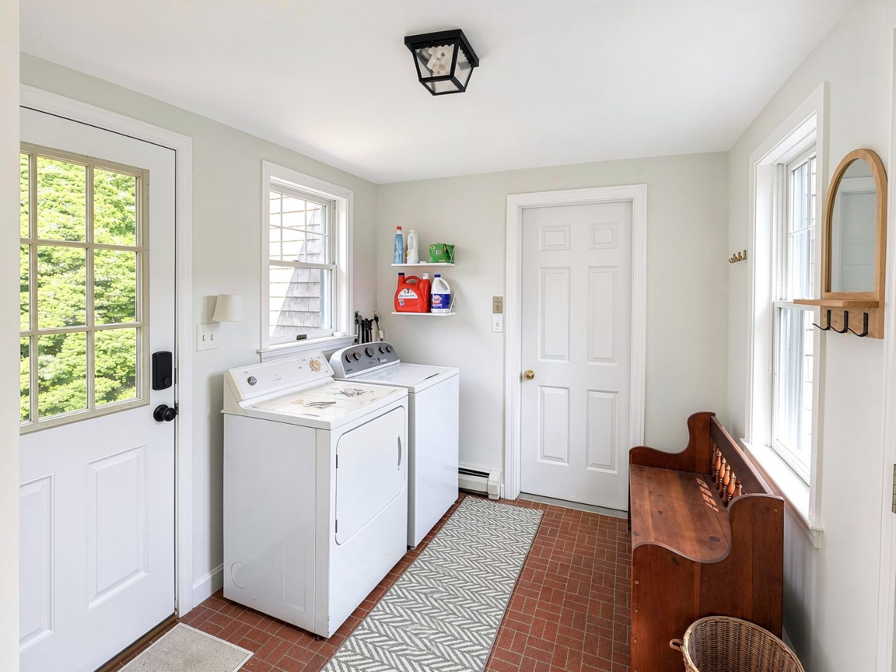 This bright laundry room blends charm with convenience. You'll find a washer and dryer side by side, shelves stocked with essentials, and natural light pouring in through crisp white windows.
