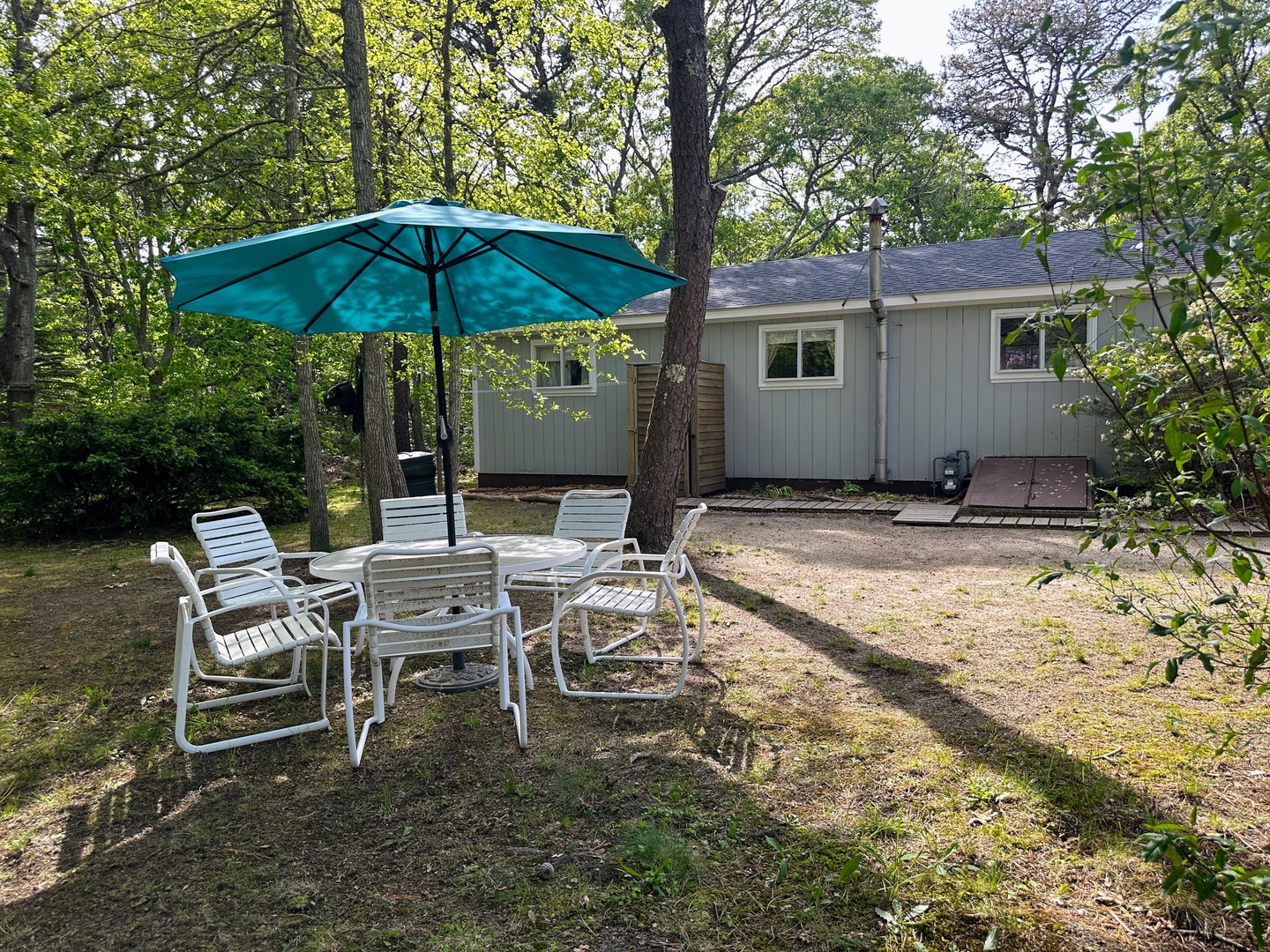 Relax in your private outdoor seating area under the shade of mature trees, with comfortable chairs and umbrella for peaceful moments.