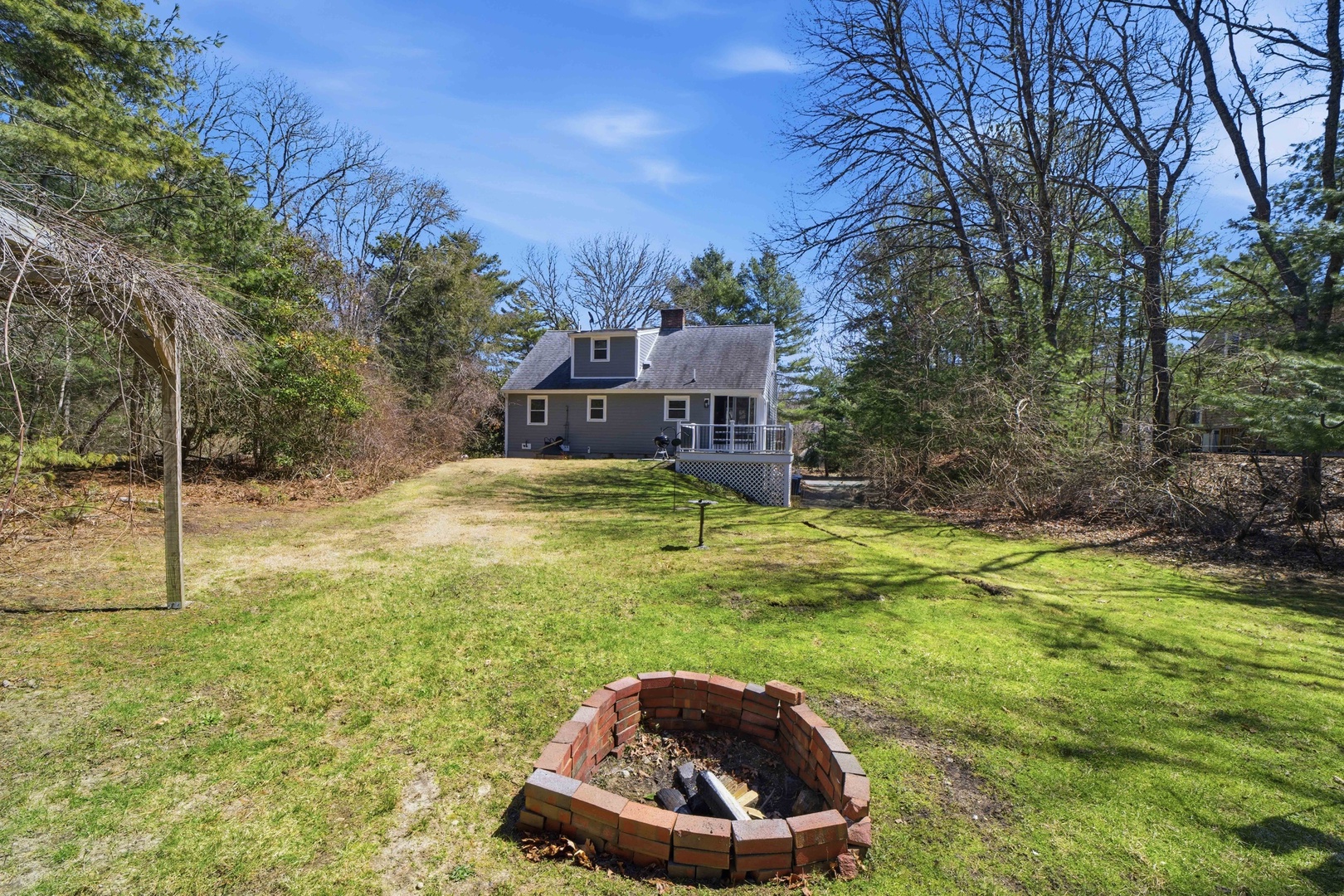 Charming cottage nestled in wooded surroundings with spacious yard and brick fire pit for cozy evening gatherings.