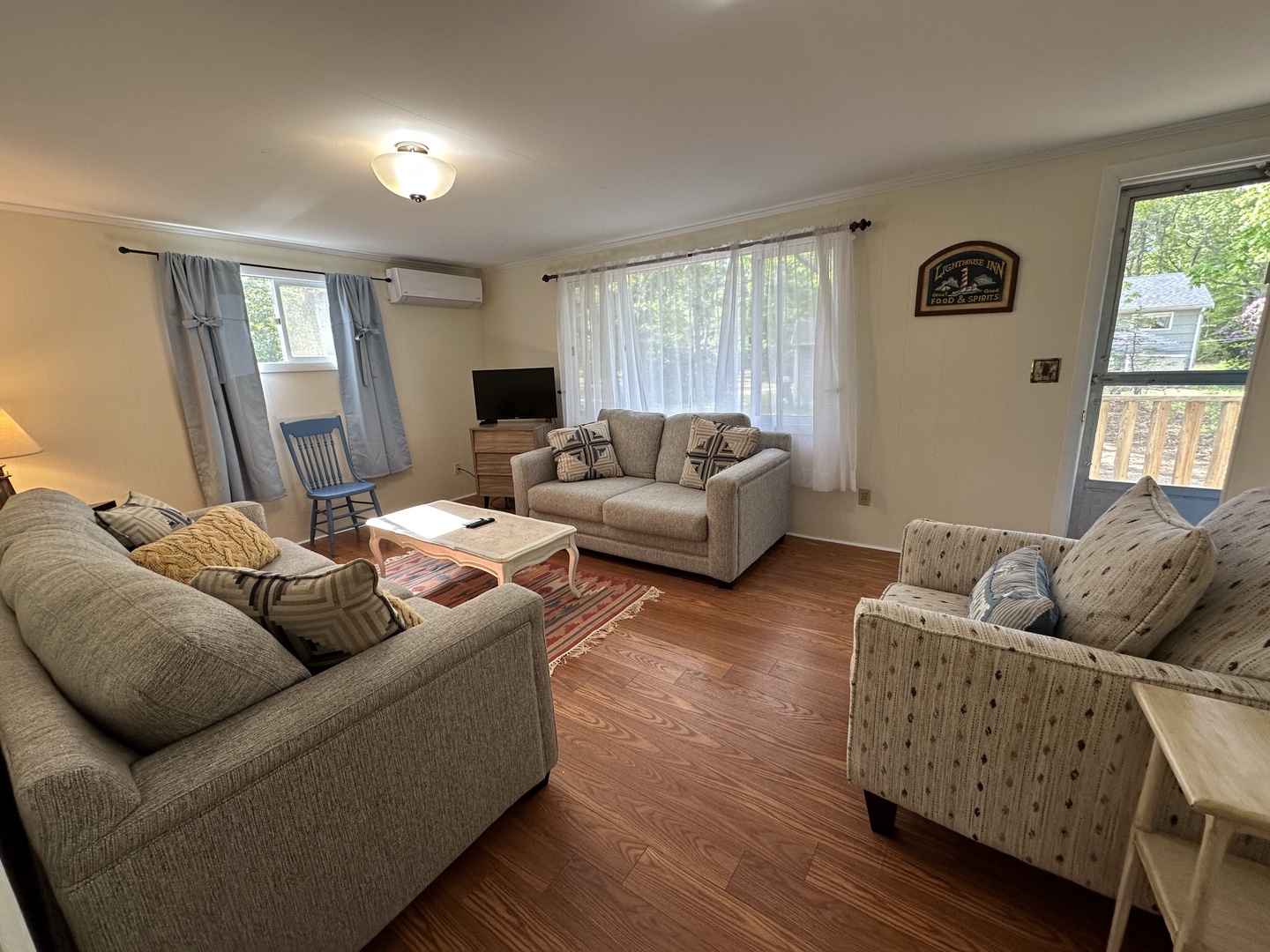 Relax in this comfortable living room with cozy seating, warm hardwood floors, and peaceful garden views through large windows.