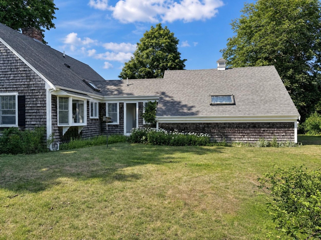 Classic shingled cottage with spacious yard, framed by mature trees and nestled in a peaceful setting—ideal for a relaxing coastal getaway.
