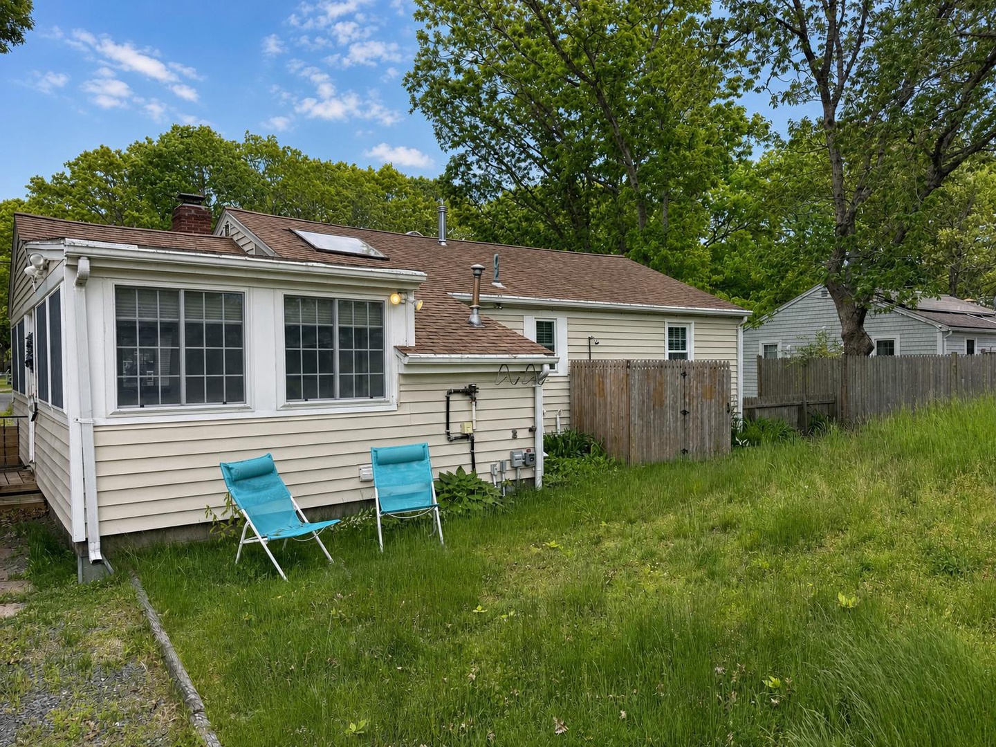 A cozy cottage nestled in a peaceful neighborhood, featuring a spacious private backyard perfect for outdoor relaxation under mature trees and open skies.