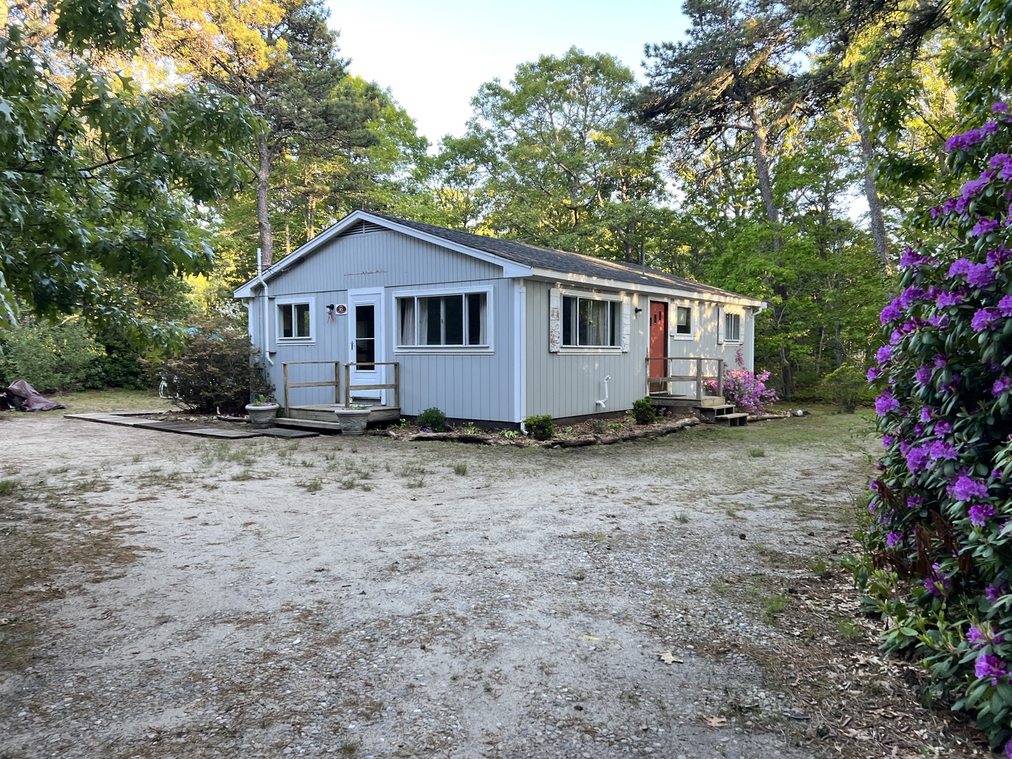 Charming cottage nestled among mature trees with colorful blooming flowers and ample parking space for a peaceful woodland retreat.