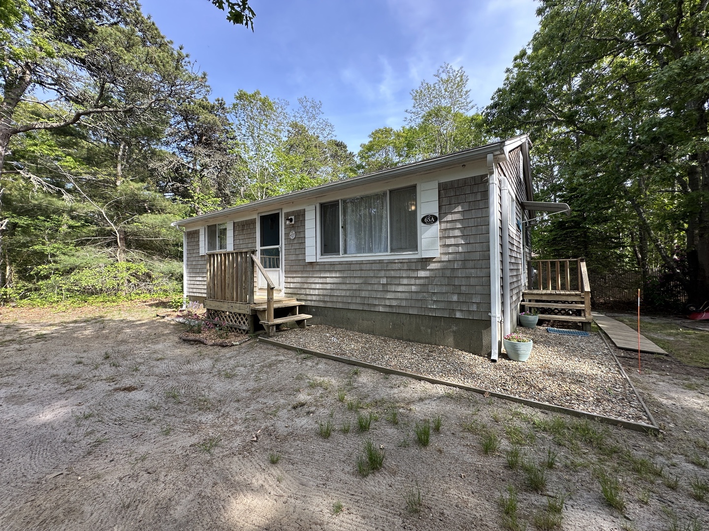 Charming cedar-shingled cottage nestled among mature trees, featuring a welcoming front deck and peaceful woodland setting for a perfect getaway.
