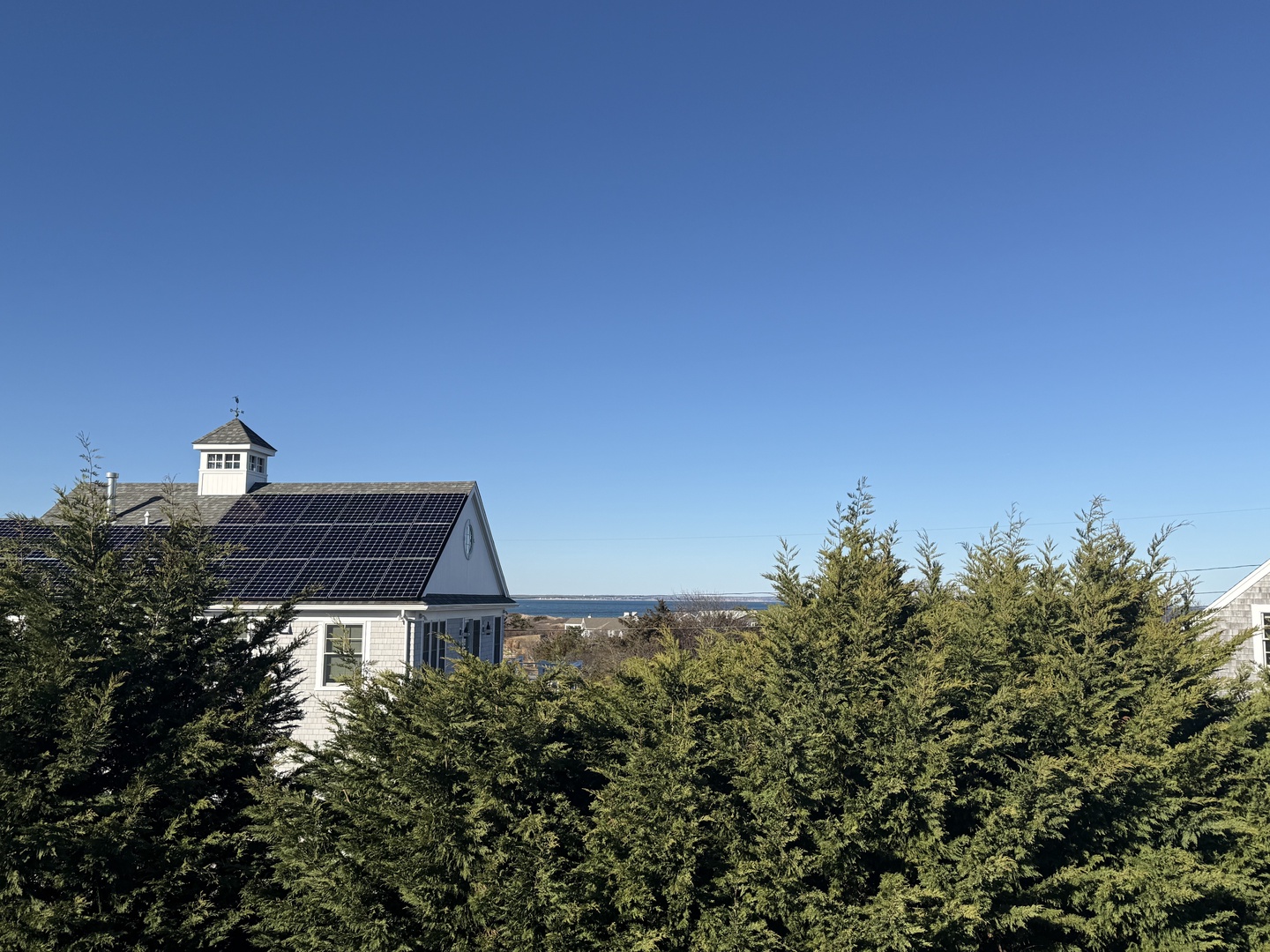 Charming coastal property nestled among evergreen hedges, offering glimpses of nearby beach and ocean beyond.