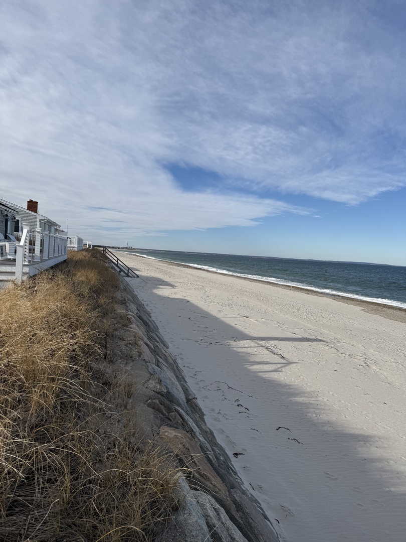 Pristine sandy beach stretches along the coastline with clear blue waters and dramatic coastal cliffs creating a stunning natural backdrop.