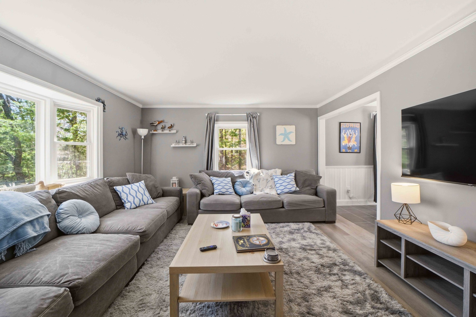 Sink into plush gray sofas while natural light filters through large windows, creating your perfect retreat for movie nights and relaxation.