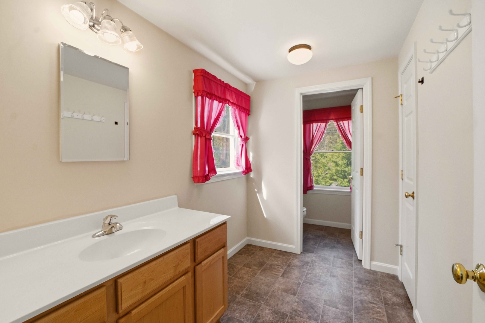 You'll love this bright bathroom with charming red curtains, modern vanity, and natural light streaming through windows.