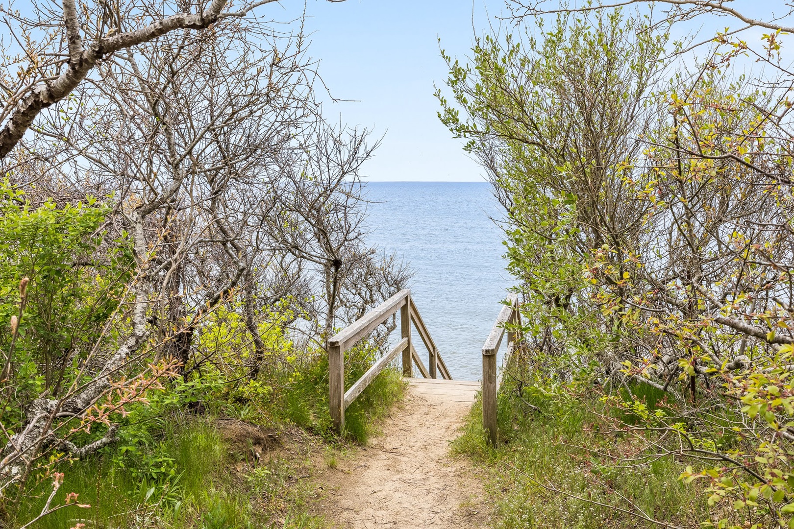 Wooden boardwalk winds through coastal vegetation toward calm waters, offering direct waterfront access from the property grounds.