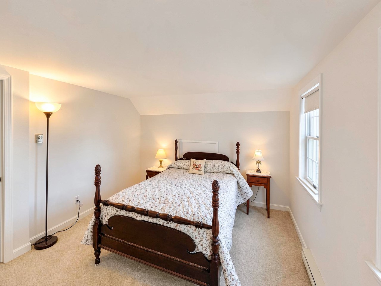 Slip into your peaceful retreat with a charming four-poster bed dressed in soft linens, where warm lighting and sloped ceilings create a cozy, restful atmosphere for your getaway.