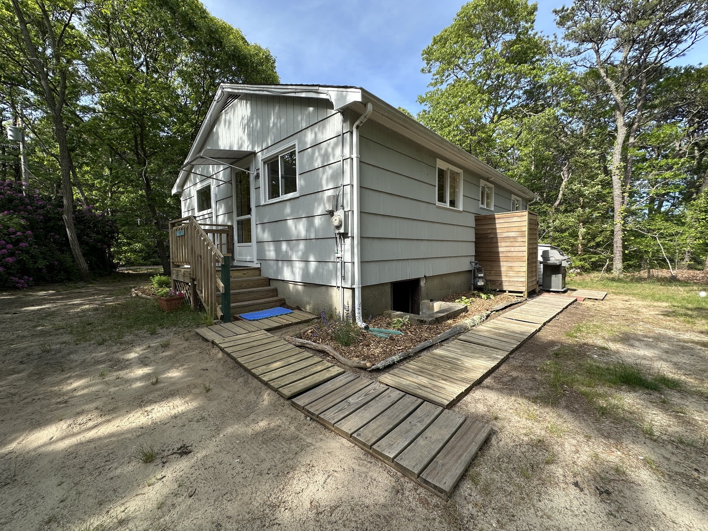 Modern vacation home nestled among mature trees, featuring contemporary siding and elevated design with wooden walkways leading to the entrance.