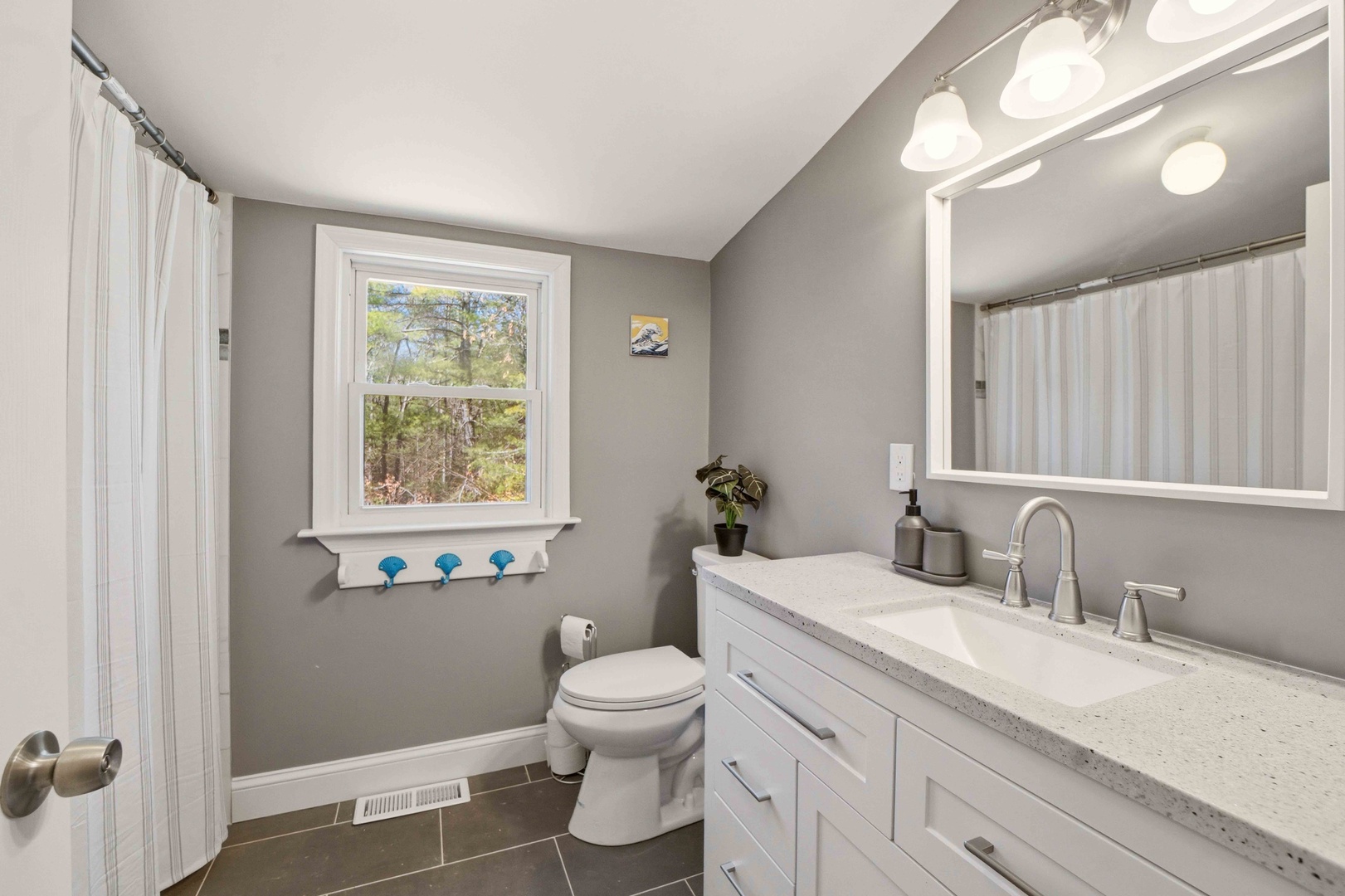Refresh in your private bathroom featuring elegant gray tones, granite countertops, and peaceful forest views through the window.