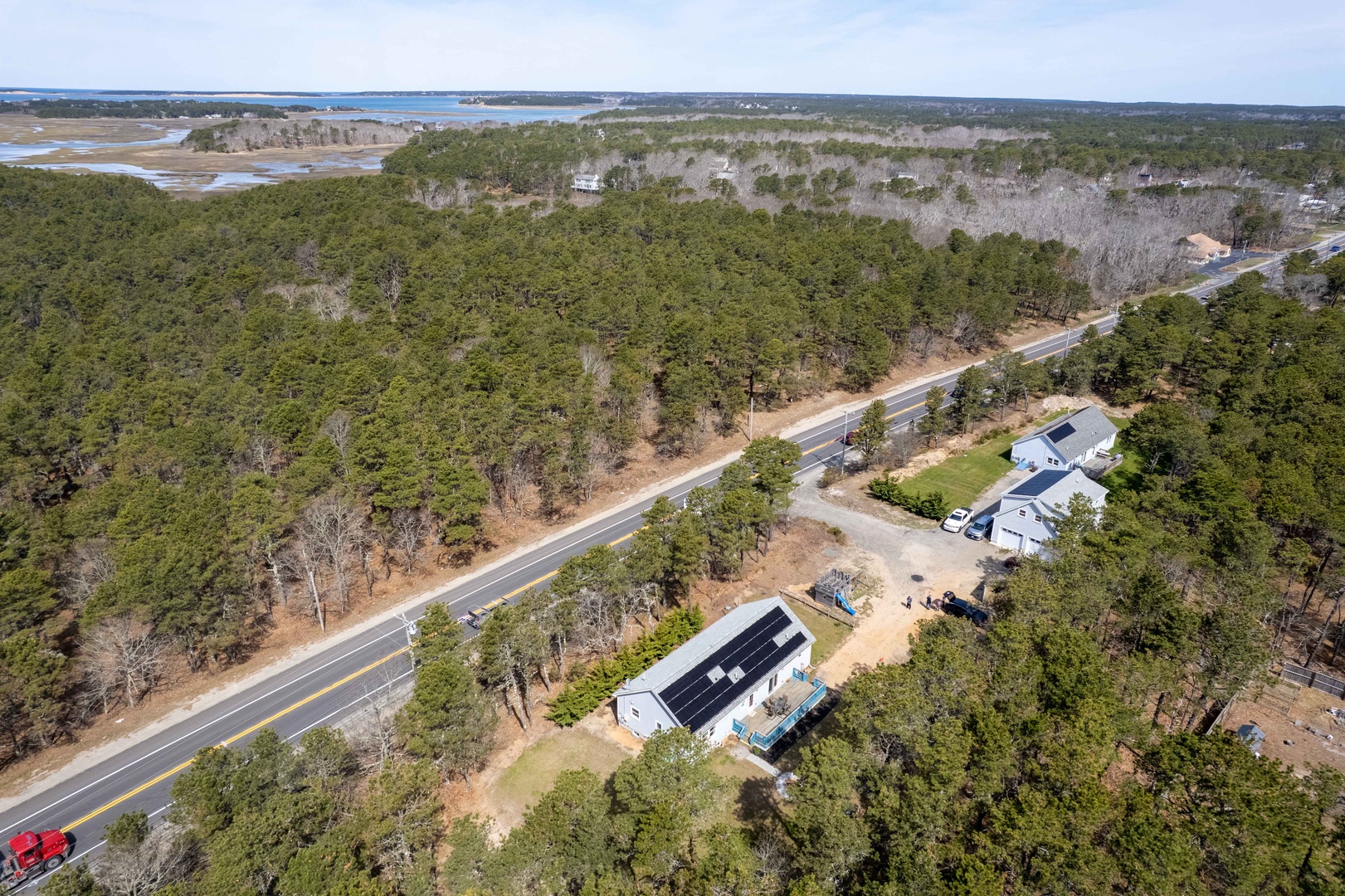 Aerial view showcases the property's peaceful wooded setting near coastal waters and local roads.