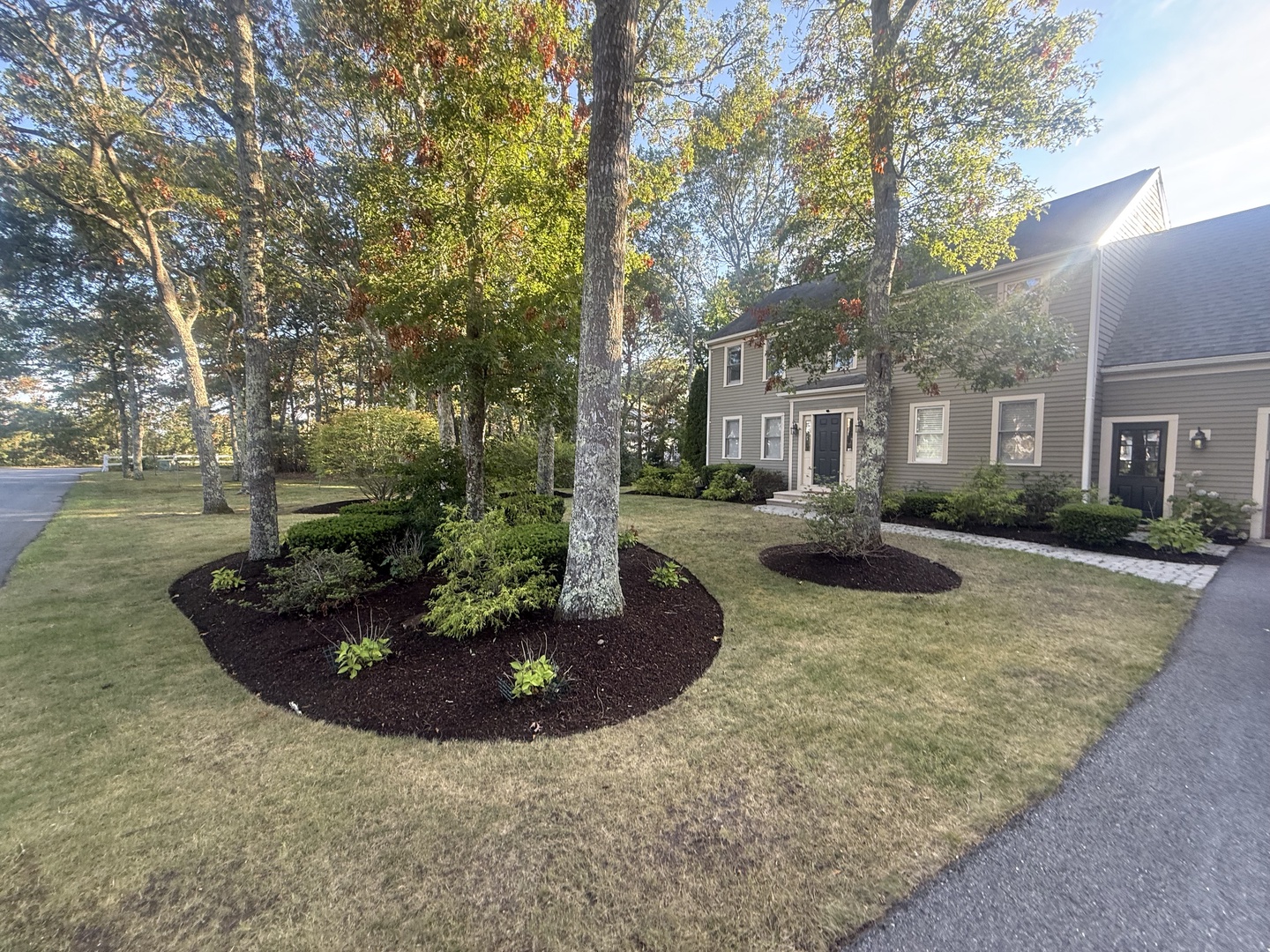 Beautiful two-story property nestled among mature trees with professionally landscaped grounds and circular garden beds creating a welcoming arrival experience.