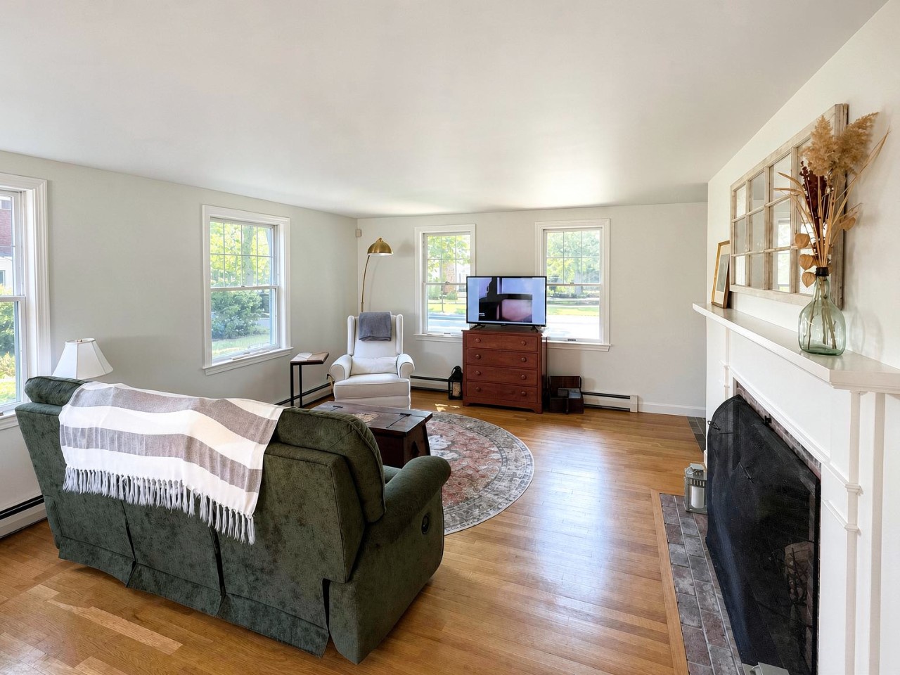 Unwind in your bright living room with warm wood floors, plush seating, and a cozy fireplace. Large windows fill the space with natural light while you relax.