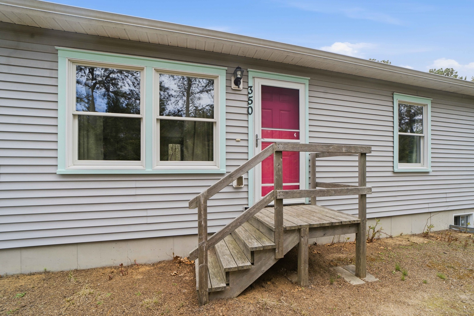 Charming gray home with distinctive red door and mint green trim, featuring wooden entry steps in a peaceful wooded setting.