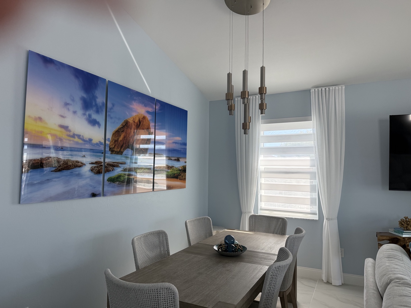 Gather around your elegant dining table beneath the stunning coastal artwork and contemporary chandelier for memorable meals together.