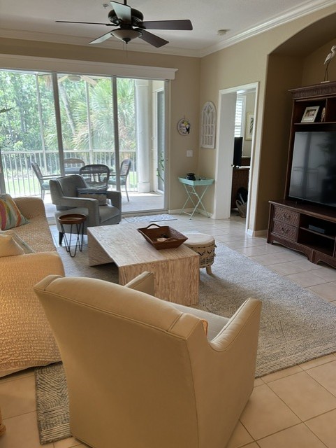Step into your bright, welcoming living room where natural light streams through large glass doors. Relax on comfortable seating while enjoying access to your private outdoor space framed by lush greenery.