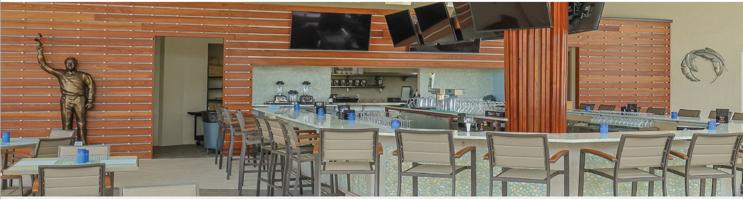 A spacious outdoor bar welcomes you with ample seating, modern televisions, and a fully-equipped serving area. The inviting space features eye-catching orange design elements that create a vibrant atmosphere for relaxation.